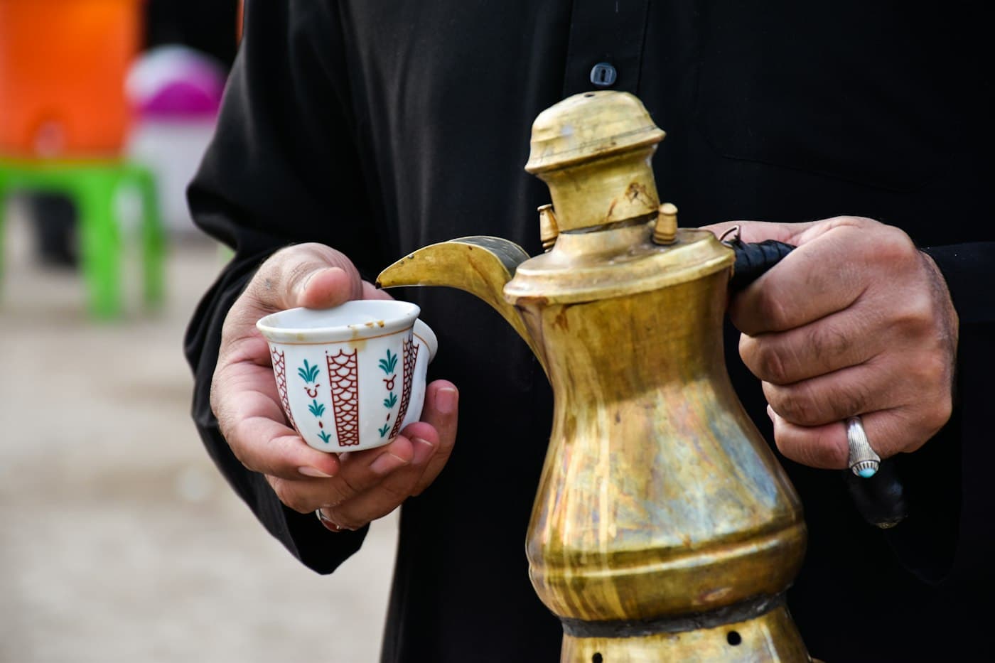 أيادٍ حول دلة قهوة نحاسية وفناجين صغيرة على طاولة منخفضة